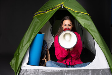 young caucasian woman inside a camping green tent shouting through a megaphone