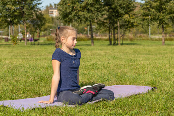 portrait of slim caucasian teenage girl doing yoga in summer city park. lotus position (padmasana). 