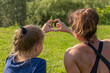 © Андрей Рыков - Photography of caucasian teenage girl and muscular woman making heart symbol with their hands in summer city park together. Mother and daughter. Healthy lifestyle. Weekend family activity theme.