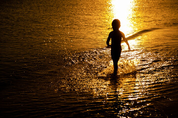 Wall Mural - Silhouette of a little girl 3-6 years old, running along the edge of the water in the sea at sunset. Recreation and sports concept