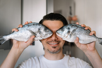 Smiling man holding raw fish in kitchen