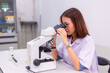 © atsarapong - Young woman researcher, doctor, scientist, looking through a microscope in a laboratory. Scientists are doing research