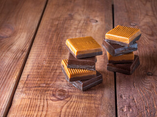 Iris candies of two colors stacked in layers on a wooden brown background close-up