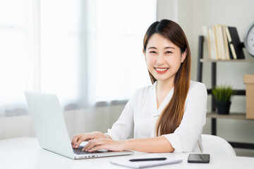 Young asian beautiful business woman working with laptop sitting at home. Smiling charming happy young female doing homework meeting conference with team at home.