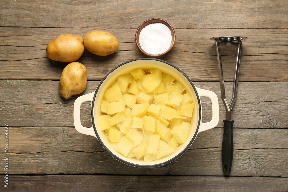 Cooking pot with boiled potatoes and masher on wooden background