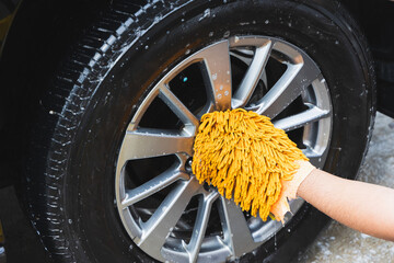 Wall Mural - The young man washed his car with foamy cleansing foam. He was wearing gloves for washing the car. He wiped the wheels of the car.