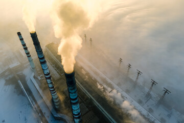 Aerial view of coal power plant high pipes with black smoke moving up polluting atmosphere at sunrise.