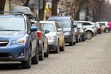 Fototapeta Kwiaty - Cars parked in a row on a city street side.