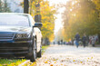 Car parked on a city street side on bright autumn day with blurred people walking in pedestrian zone.