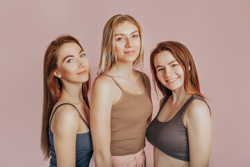 Wall Mural - three girls in comfortable home clothes together on a pink background. women smile and have fun. the