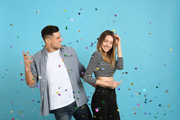 Happy couple and falling confetti on light blue background