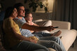 © New Africa - Family watching movie with popcorn on sofa at night