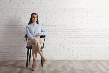 Wall Mural - Young businesswoman sitting in office chair near white brick wall indoors, space for text