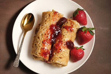 Wall Mural - Pancakeshin roll with strawberry jam on plate. Pancakes poured berry jam and decorated fresh strawberries. Top view.