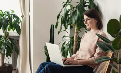 Young woman using laptop computer at home. Eco-friendly student girl working in her room. Work or study from home, sustainable lifestyle, freelance, business, lifestyle concept