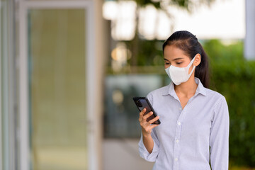 Wall Mural - Happy woman wearing face mask to protect from coronavirus Covid-19 while using phone