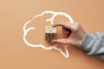 A cube in the silhouette of the brain with a picture of a smile on one side and an angry one on the other. A symbol of the choice between positive and negative in life