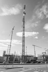 Steel cranes in a building construction site to build skyscaper. Vertical photo. Sky and white clouds on the background. Black and white.