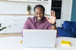 © Face Stock - Stay in touch with work team during quarantine. African-American guy using laptop for video connection, waving hi into webcam, involved video meeting with colleagues, greeting participants online