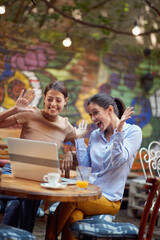 Wall Mural - Two cheerful female students are joking while have a chat on a laptop in bar's garden. Leisure, bar, friendship, outdoor