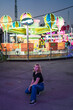 © MiguelAngelJunquera - Chica rubia guapa posando delante de atracciones de globos aerostáticos en zona de atracciones de una feria