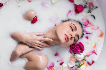 Wall Mural - seductive woman touching neck while taking milk bath with rose petals.