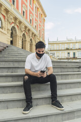 Sticker - Spanish man in a mask sitting on stairs and playing with his phone