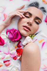 Wall Mural - top view of sensual woman touching face while taking floral bath with milk.