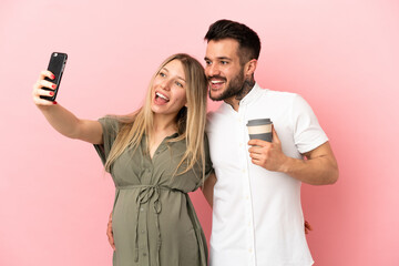 Wall Mural - Pregnant woman and man over isolated pink background making a selfie with the mobile