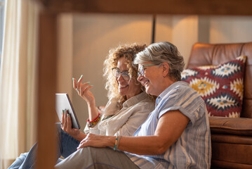 Wall Mural - adult beautiful daughter with elderly mother sitting at home looking social media on digital tablet