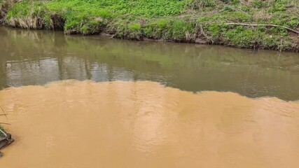 Wall Mural - Dirty orange water from sewage pipeline mixes with river water. Clear border between two different water streams. Environmental pollution theme.