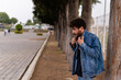 © LuisRal - Handsome young man with curly hair and beard wearing denim posing and adjusting his jacket in a public park. Close up portrait with confident expression and copy space