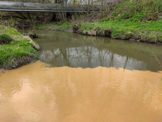 Wall Mural - Dirty orange water from sewage pipeline mixes with river water. Clear border between two different water streams. Environmental pollution theme.