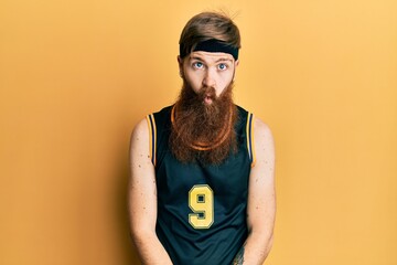 Wall Mural - Redhead man with long beard wearing basketball uniform making fish face with lips, crazy and comical gesture. funny expression.