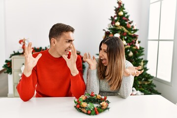 Canvas Print - Young hispanic couple sitting at the table on christmas celebrating crazy and amazed for success with arms raised and open eyes screaming excited. winner concept