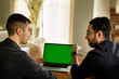 © Alla's StockPhoto - Zwei junge Männer, sehen ausländisch aus, sitzen im Wohnzimmer vom Laptop. Einer  zeigt mit dem Finger auf den Display und der anderer hört ihn gespannt zu. Der Display ist grün, green screen.