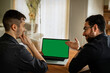 © Alla's StockPhoto - Zwei junge Männer, Anfang 20. sitzen im Wohnzimmer, schauen auf den Display eines Laptops. Einer zeigt mit den Fingern drauf,  der anderer  ist  nachdenklich. Green screen, grüner Bildschirm