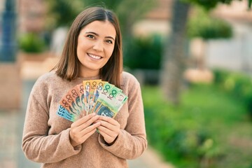 Wall Mural - Young hispanic woman smiling happy holding australian dollars at the city.