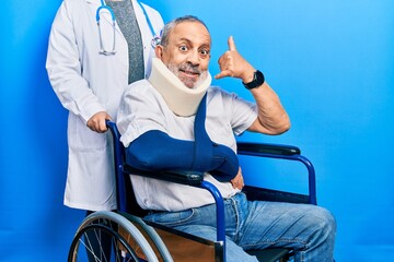 Poster - Handsome senior man with beard sitting on wheelchair with neck collar smiling doing phone gesture with hand and fingers like talking on the telephone. communicating concepts.