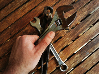 Hand of a craftsman grabbing tools such as wrench, tongs and pliers for maintenance and repair. Wooden workbench in background.	