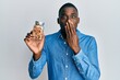 Young african american man holding jar with walnuts covering mouth with hand, shocked and afraid for mistake. surprised expression