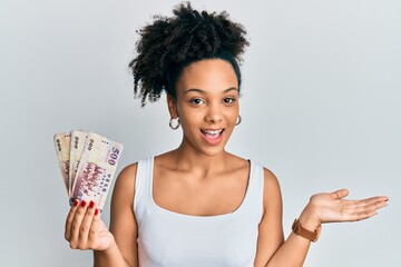 Poster - Young african american girl holding 500 new taiwan dollars banknotes celebrating achievement with happy smile and winner expression with raised hand