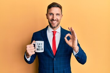 Wall Mural - Handsome business man with beard drinking from i am the boss coffee cup doing ok sign with fingers, smiling friendly gesturing excellent symbol