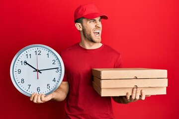 Sticker - Young caucasian man holding delivery package and clock angry and mad screaming frustrated and furious, shouting with anger. rage and aggressive concept.