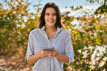 Wall Mural - Young hispanic girl smiling happy using smartphone at the city.