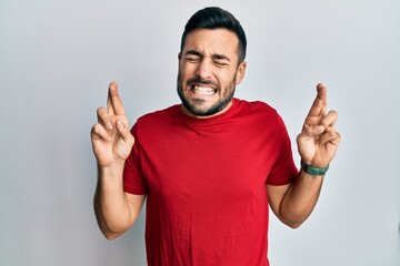 Young hispanic man wearing casual clothes gesturing finger crossed smiling with hope and eyes closed. luck and superstitious concept.