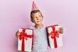 © Krakenimages.com - Adorable caucasian kid wearing birthday hat holding presents smiling looking to the side and staring away thinking.