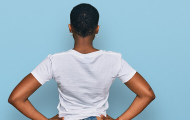 Young african american woman wearing casual white t shirt standing backwards looking away with arms on body