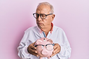 Sticker - Senior caucasian man holding piggy bank with glasses depressed and worry for distress, crying angry and afraid. sad expression.