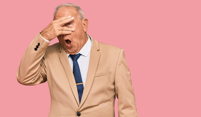 Wall Mural - Senior caucasian man wearing business suit and tie peeking in shock covering face and eyes with hand, looking through fingers with embarrassed expression.